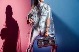 cropped view of fashionable woman in silver bodysuit and raincoat posing with boombox and disco ball